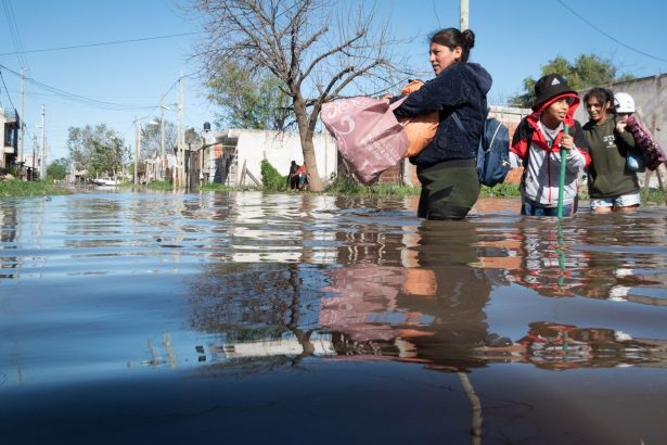 Pessoas atravessam uma rua alagada após fortes chuvas em uma área urbana.