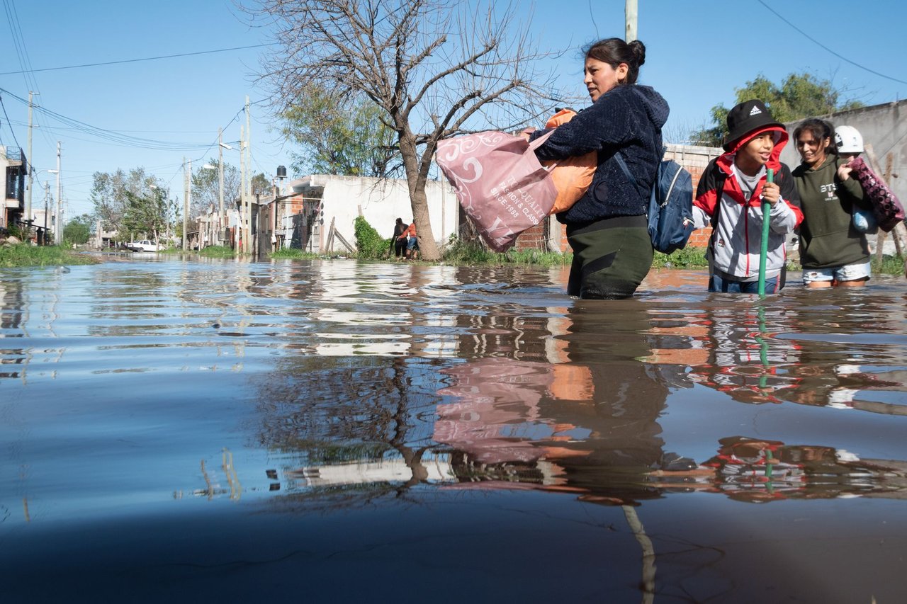 Pessoas atravessam uma rua alagada após fortes chuvas em uma área urbana.