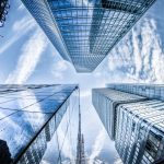Arranha-céus modernos vistos de baixo, com reflexos no céu, em um distrito financeiro.