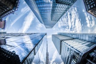 Arranha-céus modernos vistos de baixo, com reflexos no céu, em um distrito financeiro.