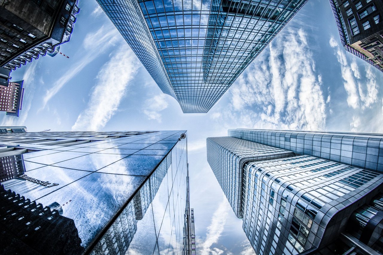 Arranha-céus modernos vistos de baixo, com reflexos no céu, em um distrito financeiro.