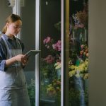 Empreendedora usando um tablet ao lado de uma exposição de flores dentro de uma loja