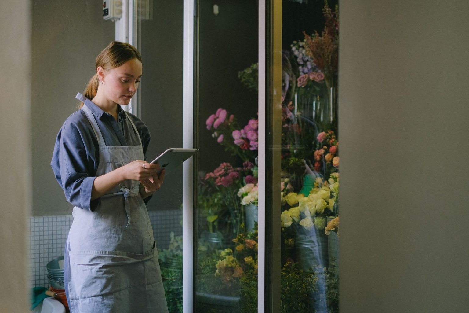 Empreendedora usando um tablet ao lado de uma exposição de flores dentro de uma loja