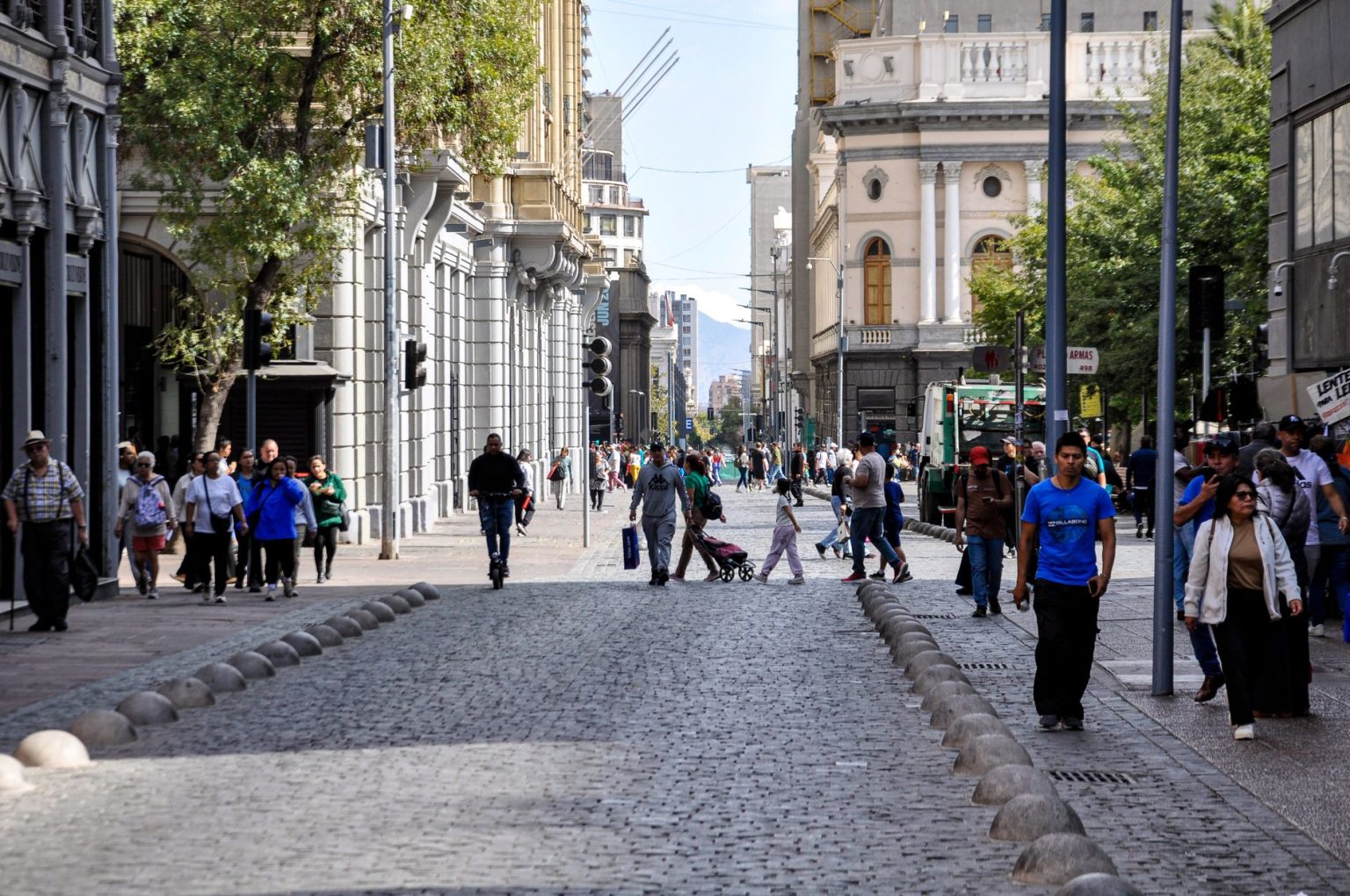 Pessoas caminham por uma rua movimentada de Santiago, no Chile, cercada por edifícios históricos.